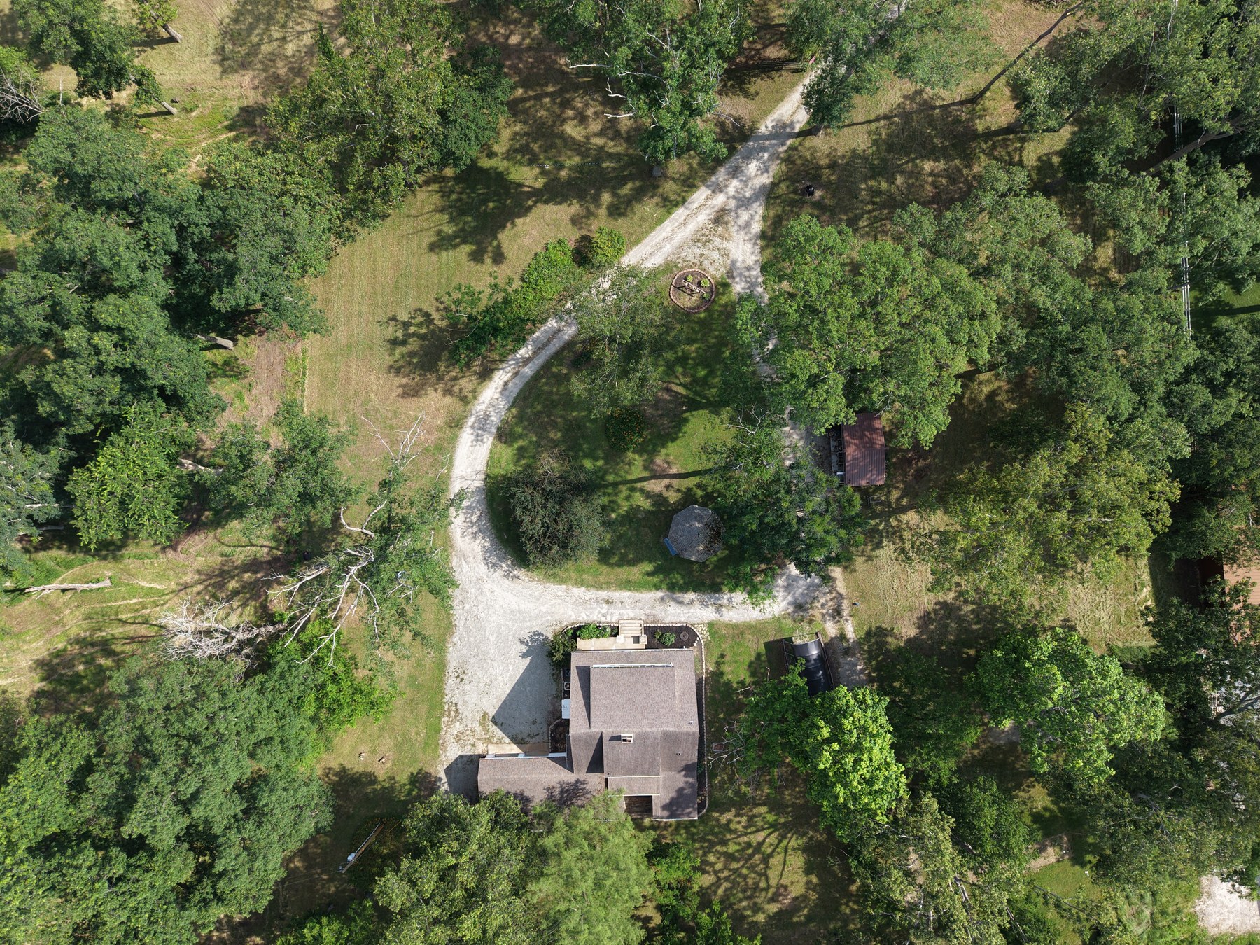 Aerial of home with looping dirt driveway in wooded lot - HelixMind Real Estate Media
