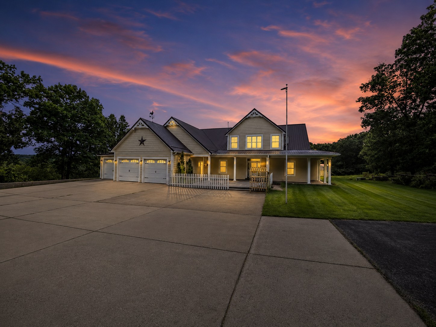 Tan farmhouse with wraparound porch on a hillside at sunset - HelixMind Real Estate Media